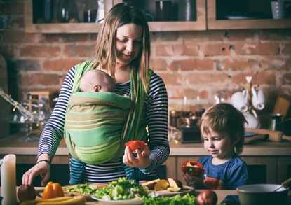 Mother teaching son to cook while holding an infant